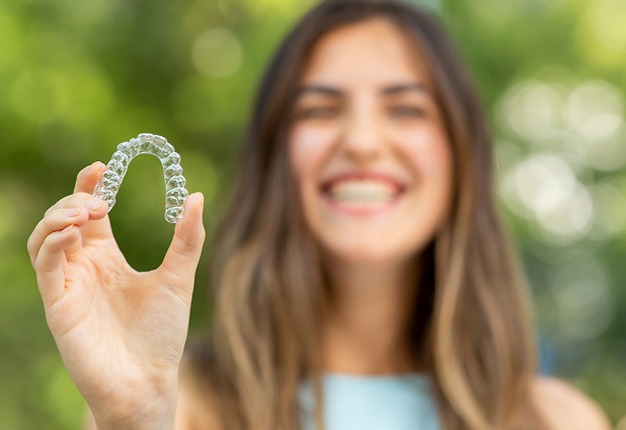 Smiling woman holding an Invisalign clear aligner