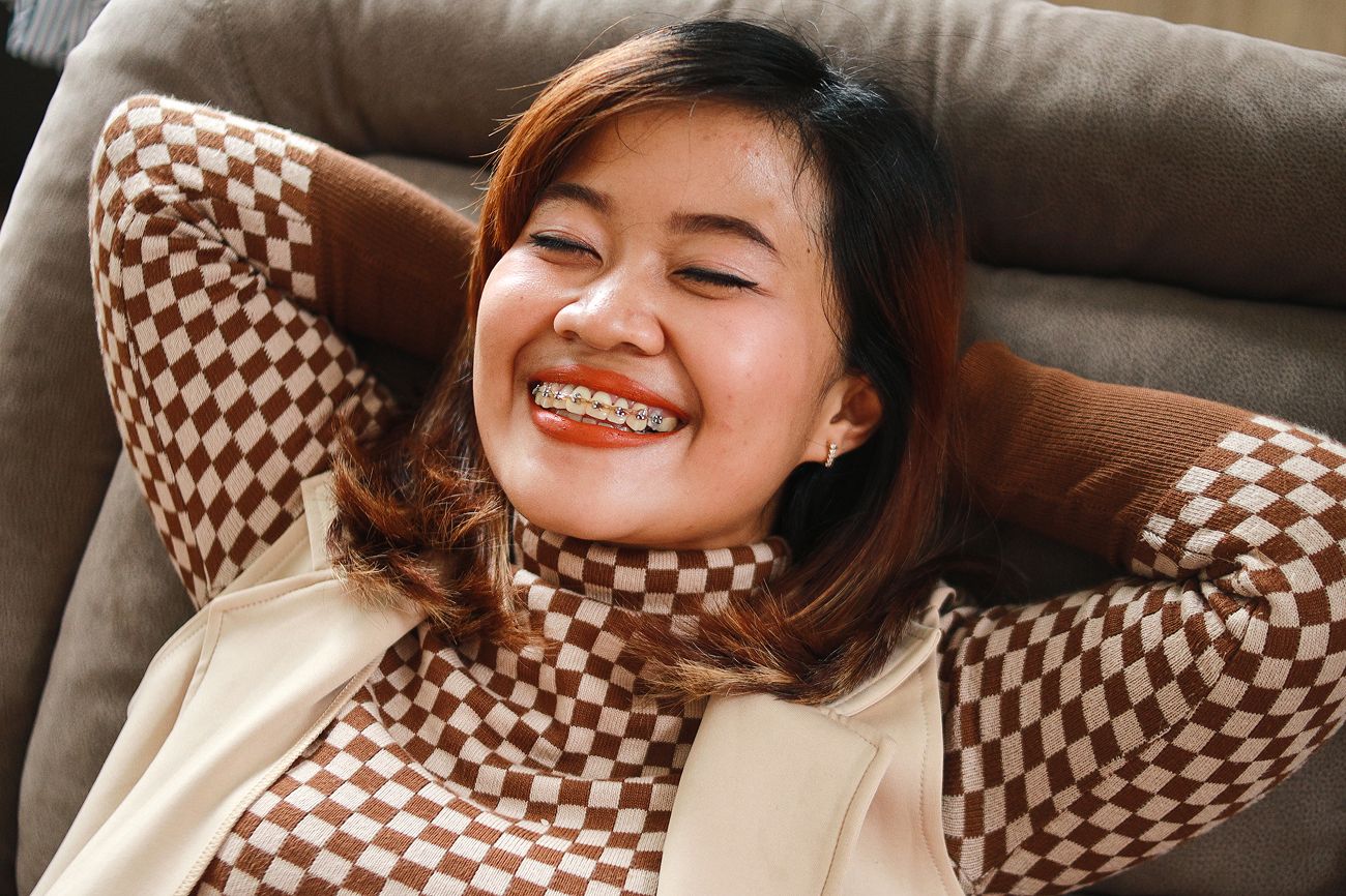 Smiling adult woman with braces relaxing on a couch, adult braces at Wire Orthodontics
